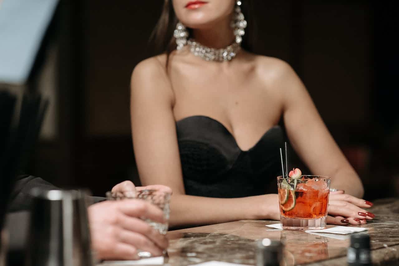 1-tinute cocktail- femeie in rochie neagra, colier si cercei, pahar in fata, maini de barbat (3)