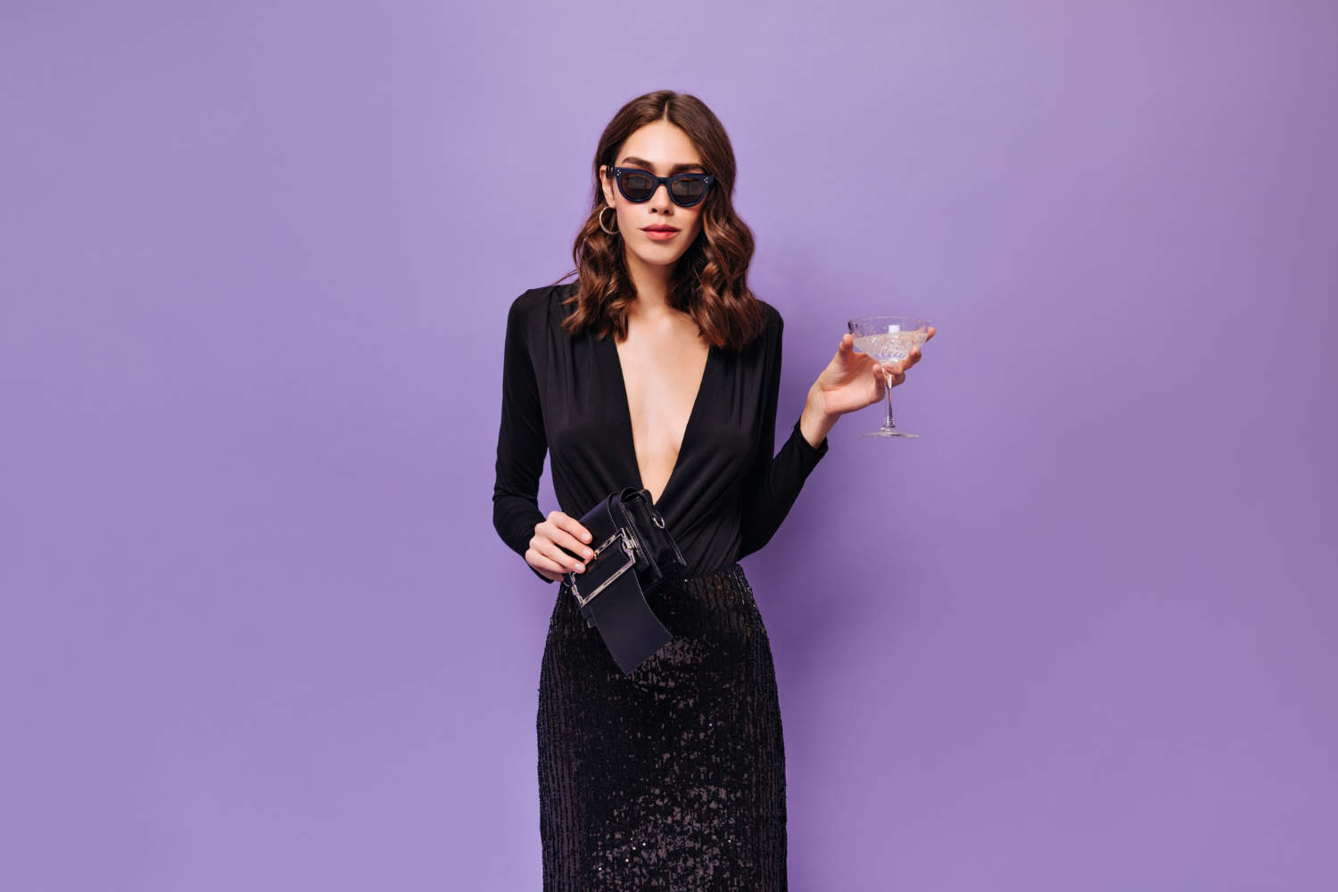 3-tinute cocktail- femeie in rochie neagra decoltata si ochelari de soare, fundal mov (9)